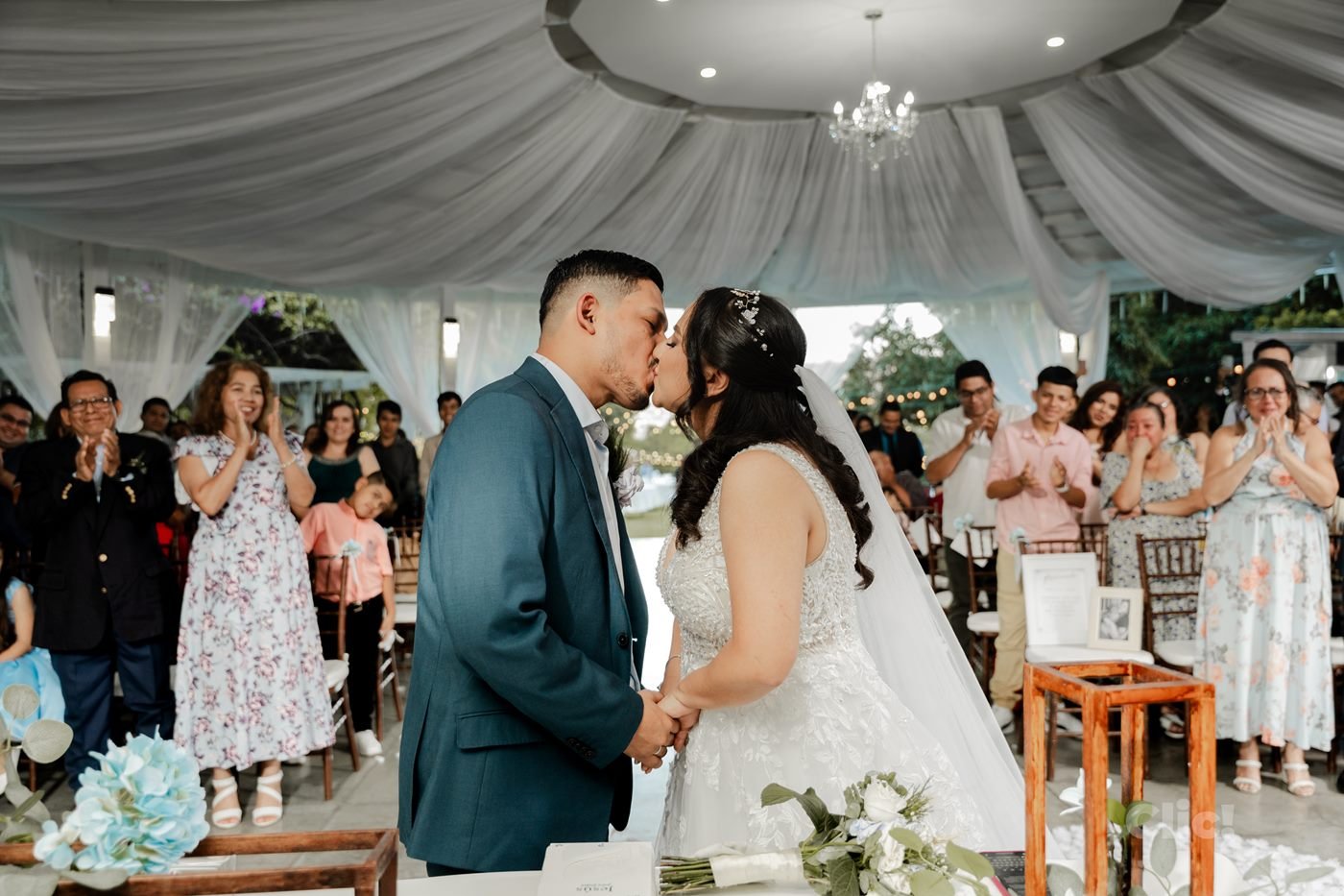 Beso de los novios en la ceremonia, entre invitados que aplauden